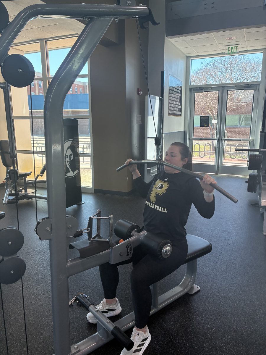 Coach demonstrating an upper body exercise (a lat pulldown) targeting shoulders and back while emphasizing correct form during a training session.
Upper body exercise including lat pulldown targets the back and shoulders, helping build upper body strength and improve posture over time. PN Photos/Sopakirite Elizabeth West. 
